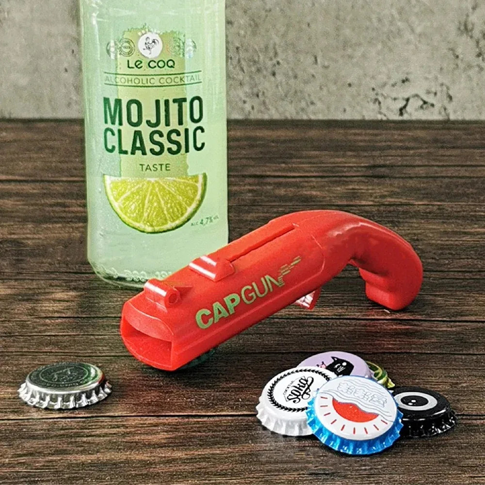 Red plastic cap gun bottle opener with nozzle, on tabletop with bottle caps